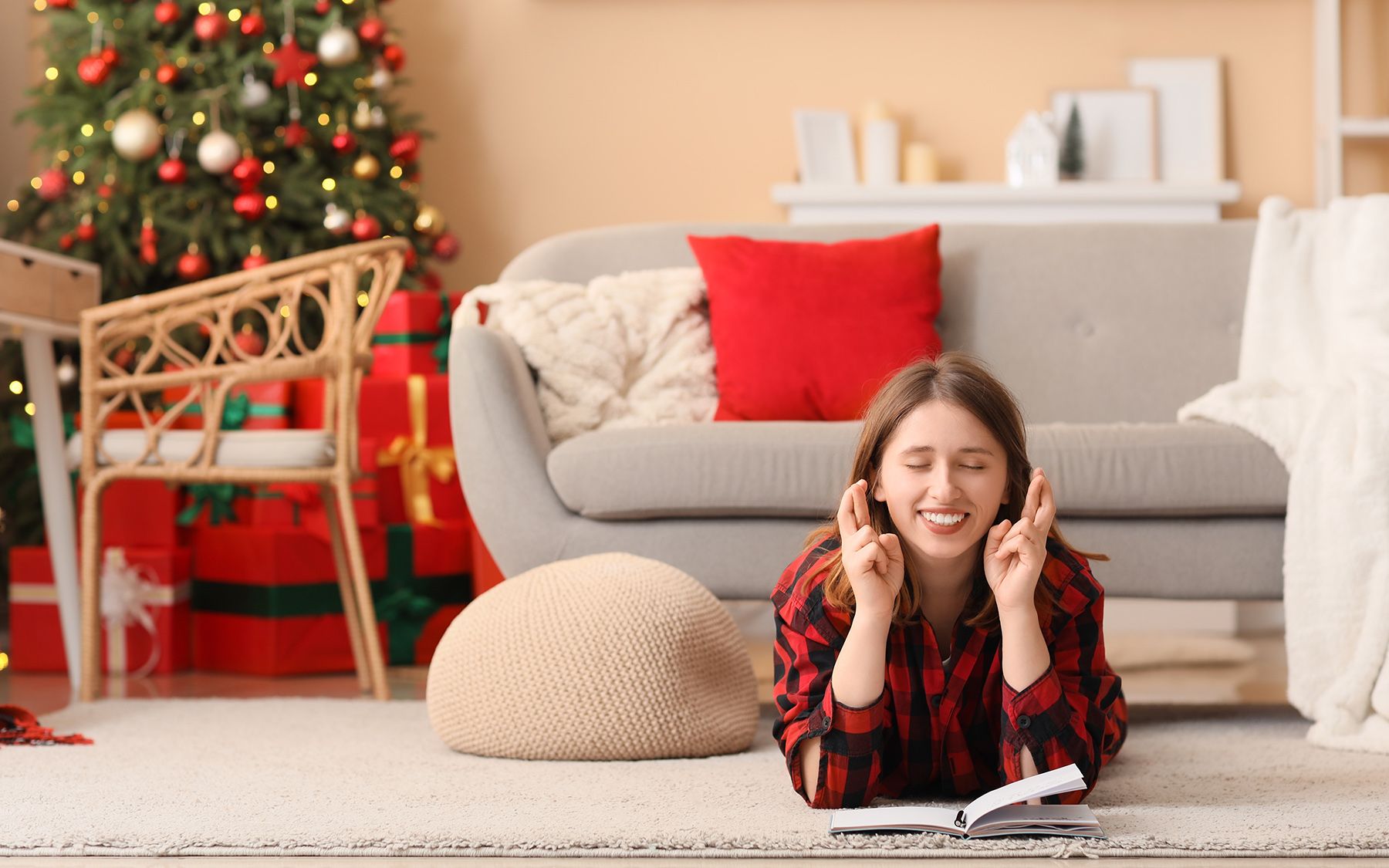 Žena dúfajúca vo vianočný darček, ležiaci na koberci v obývačke s vianočným stromčekom.