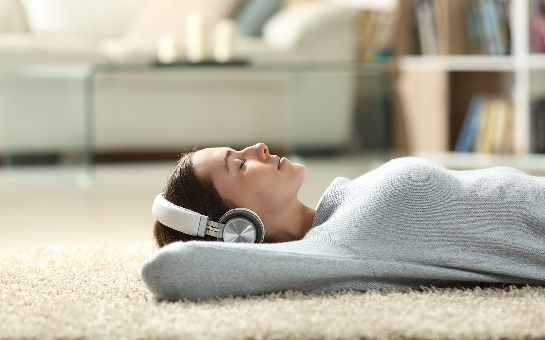 Žena ležící na zemi na koberci se sluchátky.