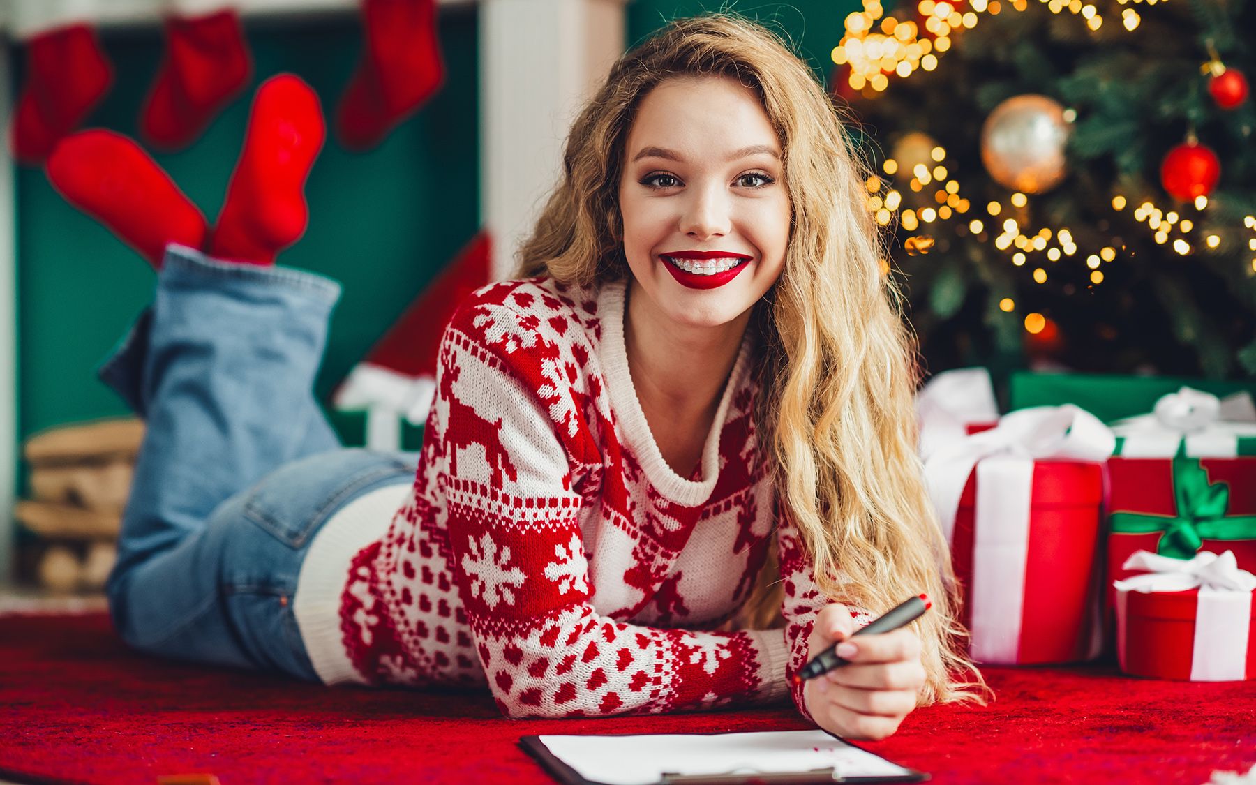 Usmívající se žena ve vánočním svetru ležící na červeném koberci.