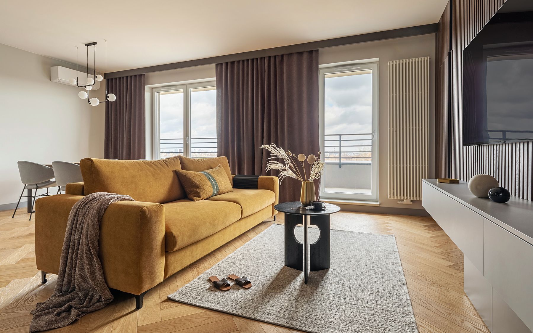 Obývací pokoj s kusovým kobercem, žlutou sedačkou a šedými závěsy.