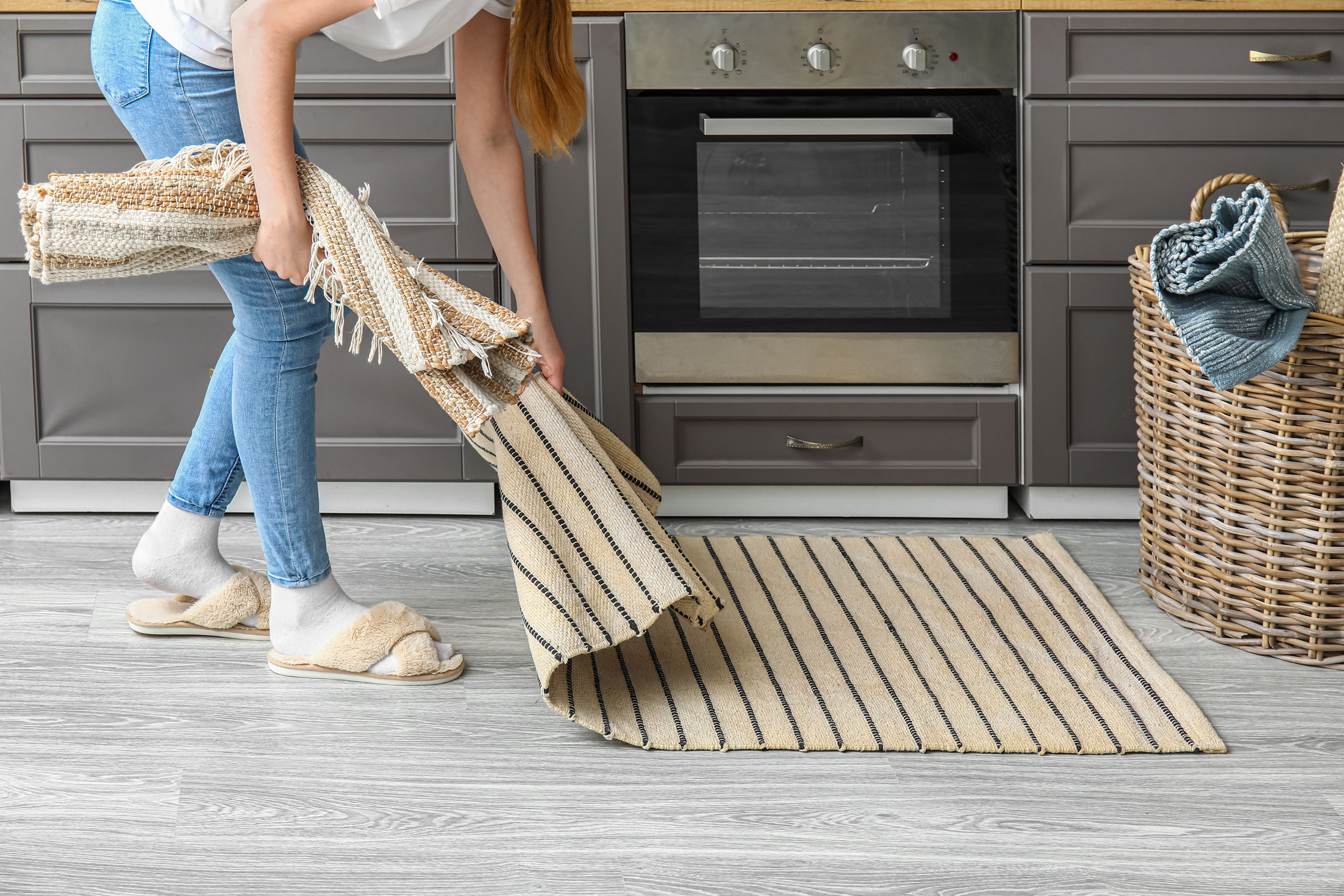 Žena při úklidu sbírá kusový koberec z podlahy před kuchyňskou linkou.