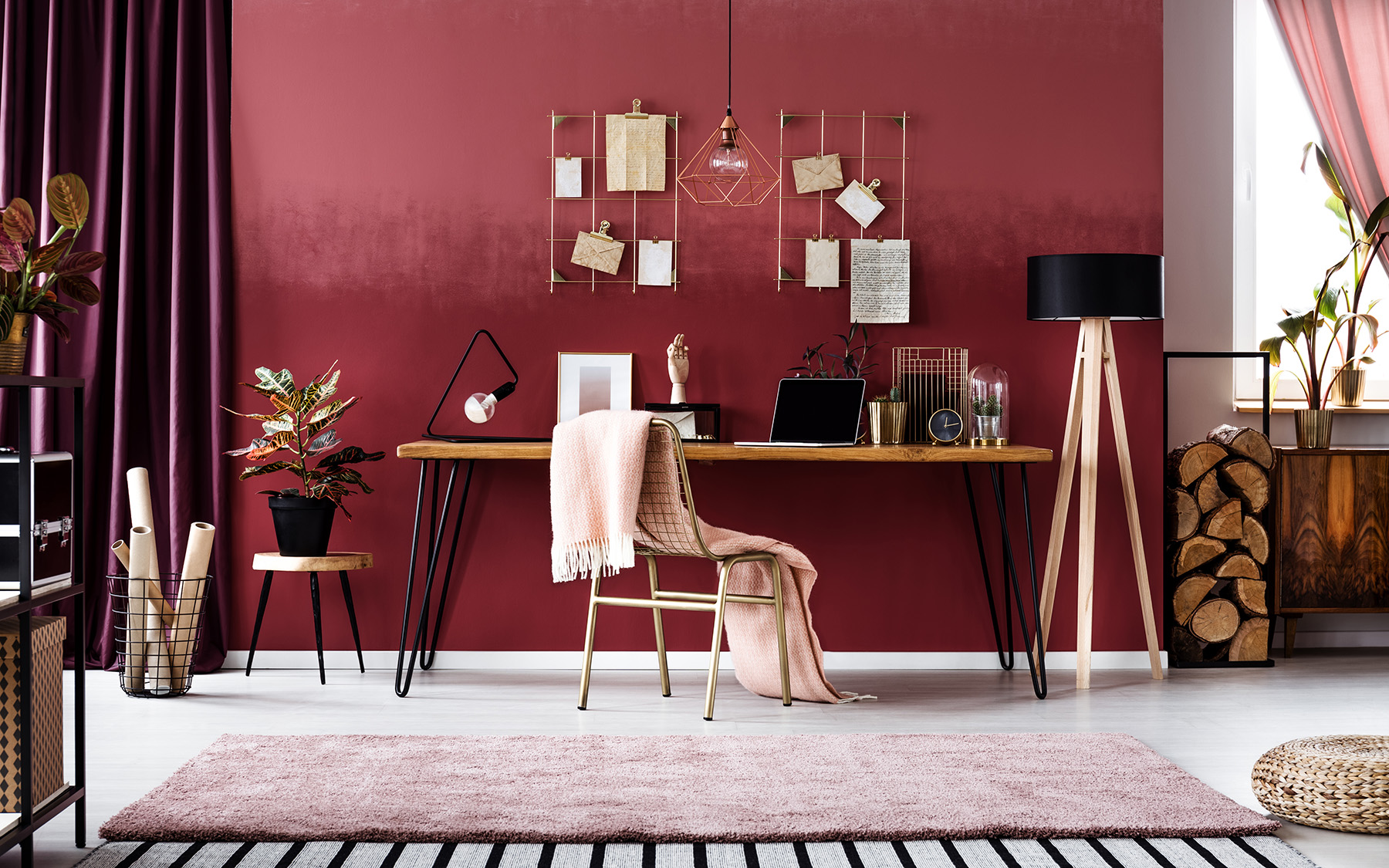 Domáca pracovňa s červenou stenou, ružovým kusovým kobercom a kovovými doplnkami.
