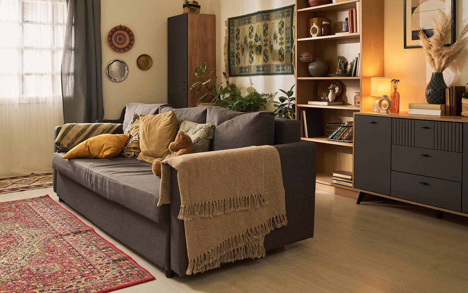 Obývák s kusovým kobercem, gaučem, polštářky a dekoracemi na stěnách i skříních.