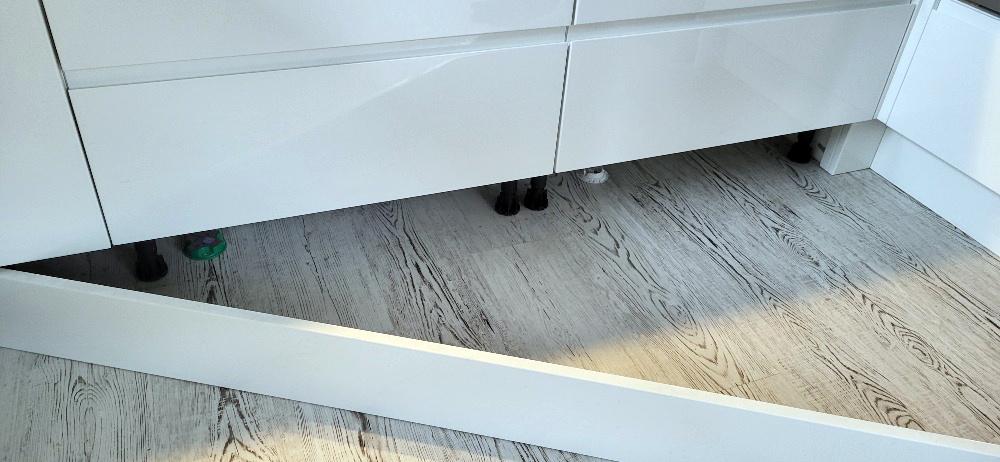 Ukázka nesprávně položeného vinylu click s absencí dilatace kolem nohou kuchyňské linky.