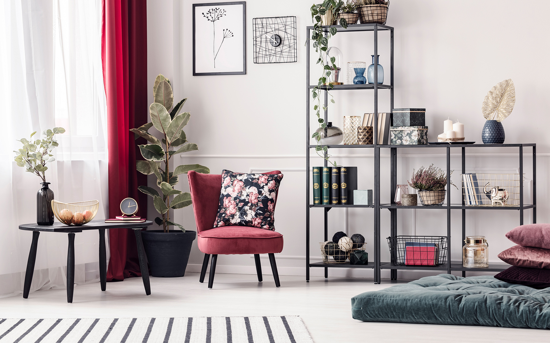 Kútik v interiéri s červenými závesmi, bordovým kreslom, kusovým kobercom a čiernym nábytkom.